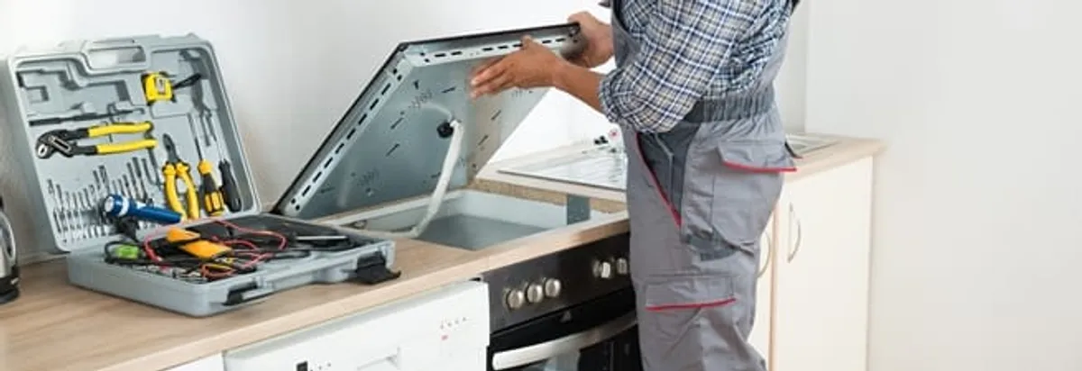 Cooktop repair technician lifting a built-in stovetop for service in Saint Louis, MO