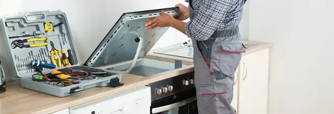 Cooktop repair technician lifting a built-in stovetop for service in Saint Louis, MO