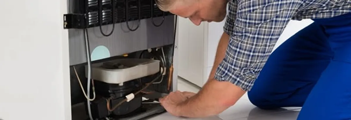 Refrigerator repair technician servicing the compressor and condenser area in Saint Louis, MO