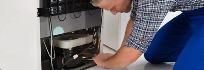 Refrigerator repair technician servicing the compressor and condenser area in Saint Louis, MO