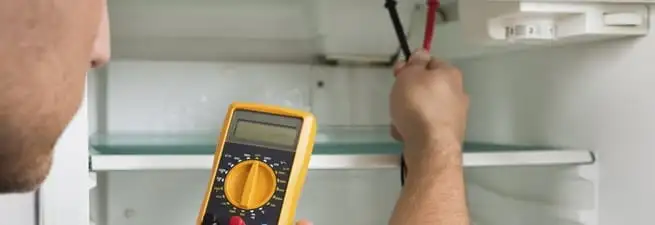 Refrigerator repair technician testing electrical components with a multimeter in Saint Louis, MO