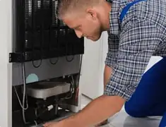 Refrigerator repair technician servicing the compressor and condenser area in Saint Louis, MO