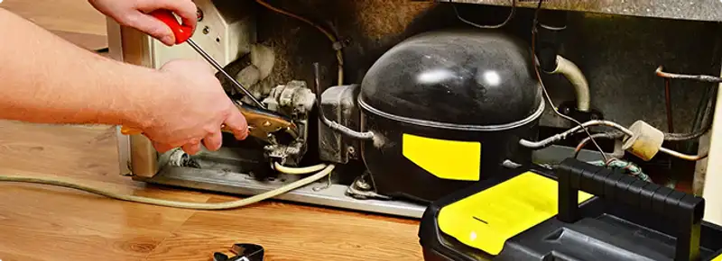 Refrigerator repair technician fixing the compressor and wiring in Saint Louis, MO